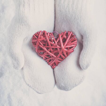 Woman hands in  knitted mittens are holding a beautiful entwined vintage romantic red heart in a snow background.の写真素材
