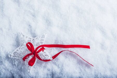 Beautiful magical vintage white star tied with a red ribbon on a white snow background.の写真素材