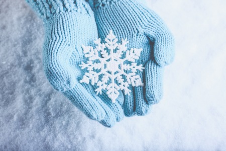 Female hands in light teal knitted mittens with sparkling wonderful snowflake on a white snow background.の写真素材