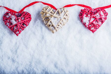 Three vintage hearts are hanging on a red band on a white snow background.の写真素材