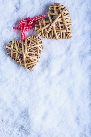 Two entwined beige flaxen hearts tied together with a ribbon on white snow.の写真素材