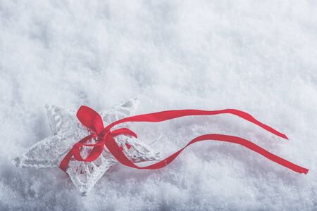 Beautiful magical vintage white star tied with a red ribbon on a white snow background.の写真素材