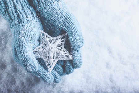 Female hands in light teal knitted mittens with entwined white star on a white snow background.の写真素材