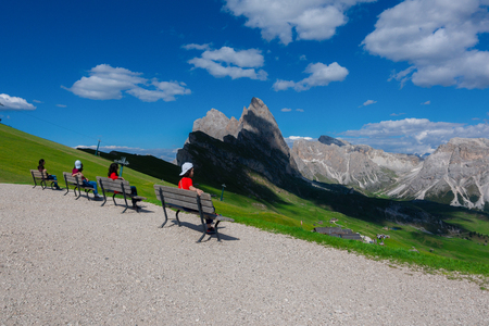 Young travelers on the bench in row with the background of Seceda peak, Val Gardena, South Tyrol, Italy.のeditorial素材