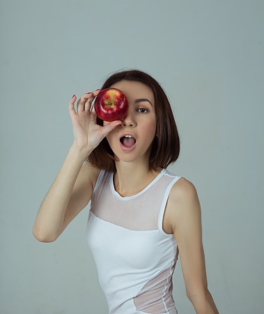 A girl with an apple standing against neutral backgroundの写真素材