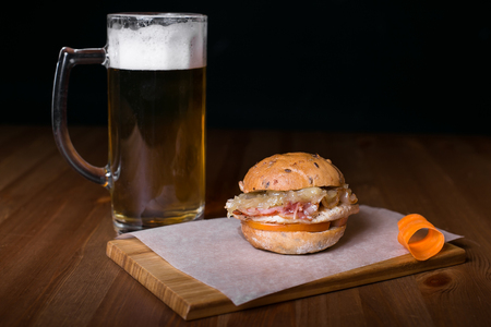Fresh homemade burger with in old metal plate with fried potatoes in baking paper, served with glass of cold lager beer over old wooden table with dark background. Dark rustic style.の写真素材