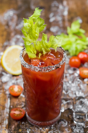 Cocktail spicy Bloody Mary with ice in glass on a wooden table decorated tomatoes, lemon and ice cube. Alcoholic Drinkの写真素材