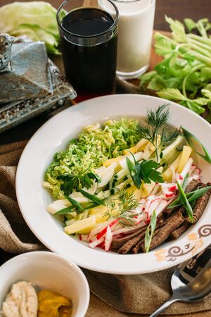 Traditional Russian summer Cold Soup Okroshka with kefir and kvass serving size in bowl and ingredients on wooden tableの写真素材