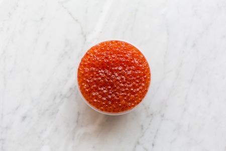 Top view of red caviar in a bowl on a light marble background