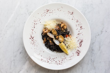 Black pasta served with seafood. Black noodles with mussels, squid, octopuses with the addition of Parmesan cheeseの写真素材