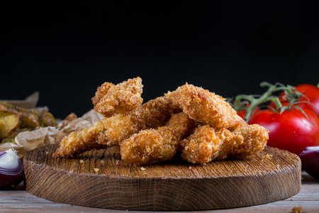 Chicken breast nuggets with vegetables on wooden background. Pile of crispy homemade baked chicken nuggets cooling.の写真素材