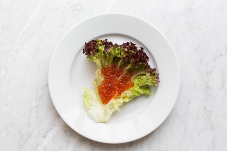 Top view of red caviar on a salad leaf on a light marble background. copy space, Top viewの写真素材