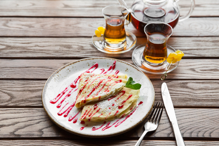 Delicious thin pancakes served with strawberry sauce on a wooden rustic tableの写真素材