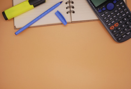 Top view note book with calculator highlighter and pen on orange background with copy space...