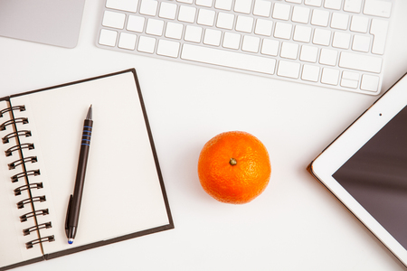 An opened notebook, a keyboard, a pad and a mandarin on the table, workplace backgroundの写真素材