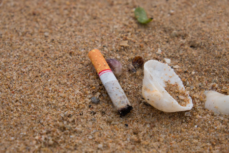 Closeup discarding cigarette butts waste is dumped on the beach. Cause dirt pollution to nature and...