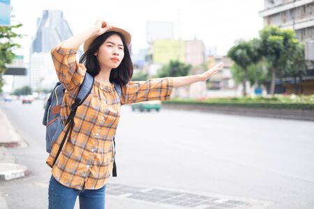 Asian girl tourists Standing on the roadside To wave a taxi for travel in the capitalの写真素材