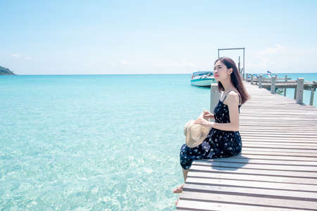 Asian woman tourists Sitting on a wooden bridge at the beautiful sea view. the clear skies with clouds. Is a tourist destination that is perfect for relaxing on holidays.の写真素材