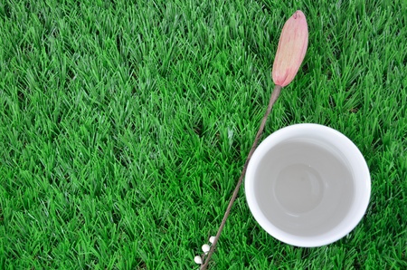 A glass with artificial flowers on the grass backgroundの写真素材