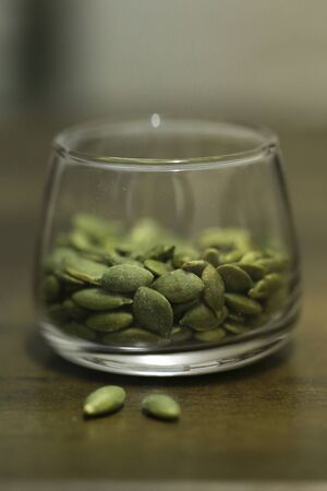 Pumpkin seeds in the glass bowl over wooden background close upの写真素材