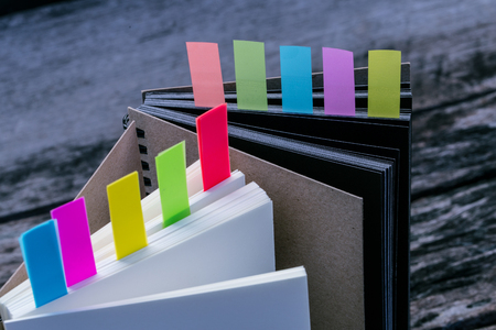 Closeup shot of notebook with color note tab. Notebook with colors note tab on wooden table background, Vintage picture tone.の写真素材