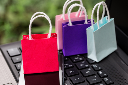 Colorful paper shopping bags with mobile phone on a laptop keyboard. Concept about online shopping that customers can buy everything from home or office. Via the tool electronics.の写真素材