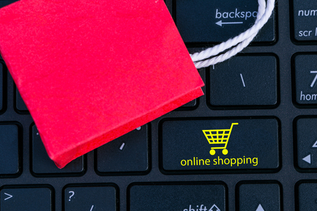 Red paper shopping bag on notebook keyboard. concept about online shopping. e-commerce or electronic commerce is a transaction of buying or services online over the internet just search and clicks.の写真素材