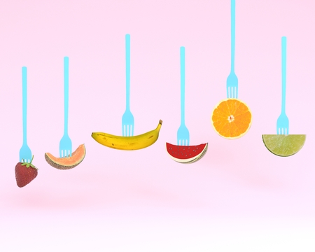 Creative layout made of fruits on the collection of forks on pastel pink background. minimal idea summer tropical fruits, diet healthy eating conceptの写真素材