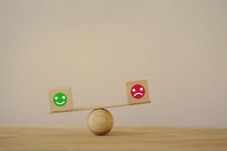 Satisfaction survey concept: Symbol icon smiley face and a sad face on wood block cube a balance...