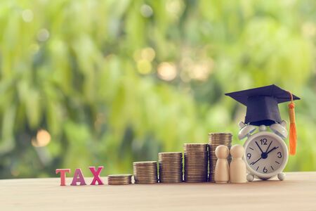 Black graduation cap, hat, student and kid, rows of rising coins, white clock on a table, natural green background. Public school funding, education funding, financial conceptの写真素材