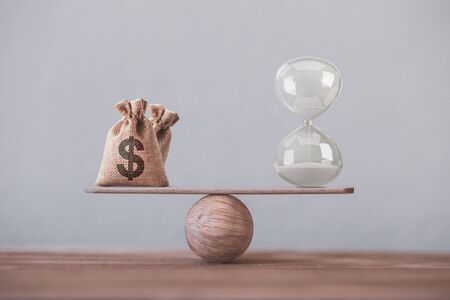 Write sand clock or hourglass symbol and dollar bagson a balance scale in equal position. Financial concept : Time value of money, asset growth over time, depicts investment in long-term equity for more money growthの写真素材