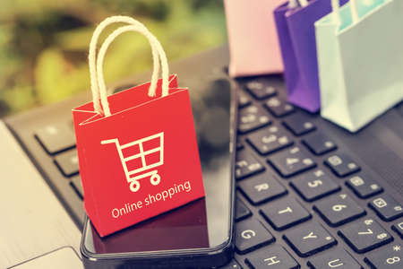 Business concept : red small paper shopping bags with smartphone on notebook keyboard. Online shopping or order goods on the internet It is more popular. can buy everything from home or office.の写真素材
