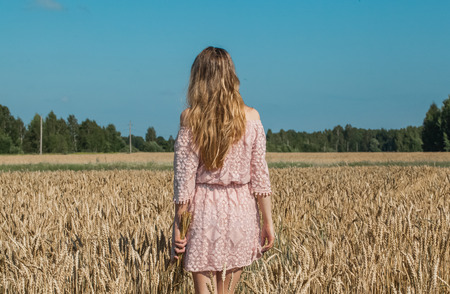 Girl walking on the field with wheatの写真素材