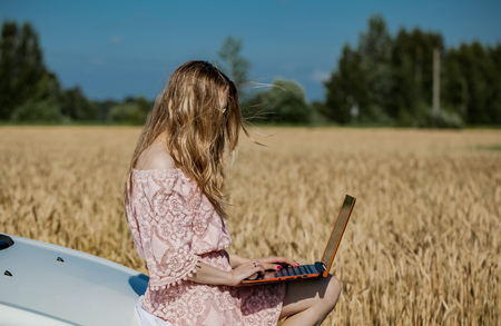 Girl working on a laptop near the field with wheatの写真素材