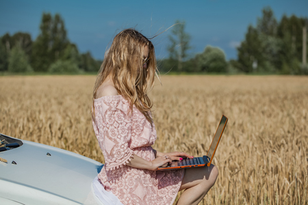 Girl working on a laptop near the field with wheatの写真素材