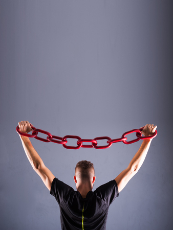 One young man in a black chain raises above his head. The concept of freedom, or sports. Free spase for comercial Grey background with room for textの写真素材
