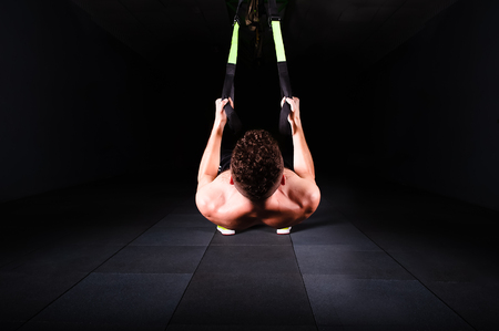 One young handsome brave curly bearded muscled man with a beard makes Total Resistance eXercises fitness trx straps working out in gym crossfitの写真素材