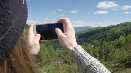 A woman is taking pictures against the background of big mountains and the green mountain river. on...