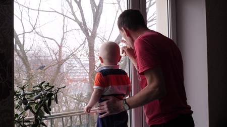 An old man and his adorable little grandson are playing by the window and grandfather show to the baby boy a bird on the tree behind the window in slow motion middle shot 4K indoor videoの写真素材
