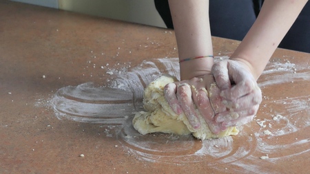 Female hands kneading dough in flour on table