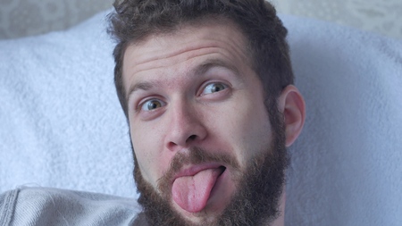 A young bearded man poses a face showing tongue hamming smiling and laughing closeup