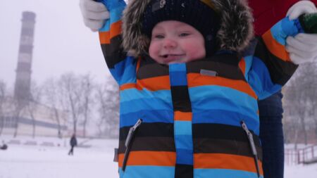 Mother leads the hands of a small smiling baby in the snow in the park. The first steps of the child. Parental careの写真素材
