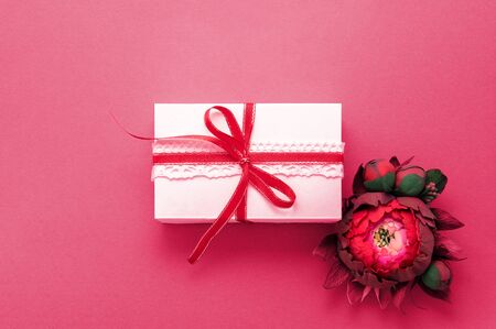 Gift box present decorations flatlay. White gift red ribbon pink flowers top view. Congratulation template banner frame white box pink paper copy space backdrop mock up invitation design greeting cardの写真素材