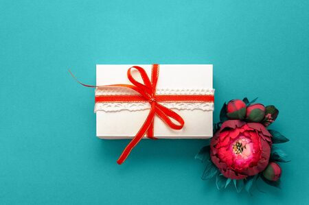 Gift box present decorations flatlay. White gift red ribbon pink flowers top view. Congratulation template banner frame white box blue paper copy space backdrop mock up invitation design greeting cardの写真素材