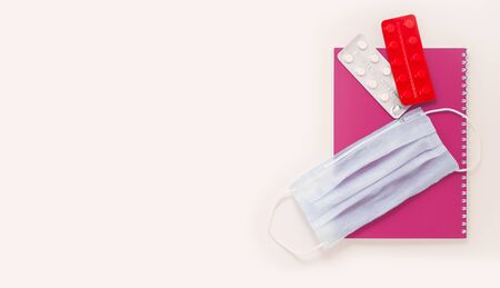 Stay at home white background flatlay. Home office medical mask pink notebook red white tablets pills strips top view template long banner. Copy space backdrop mock up. Distance education work conceptの写真素材