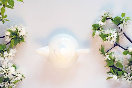 White tea pot, apple tree blossom branch, white background flat lay. Flowering buds top view template long web banner. Copy space backdrop mockup design. Floral spring frame flowers invitation conceptの写真素材
