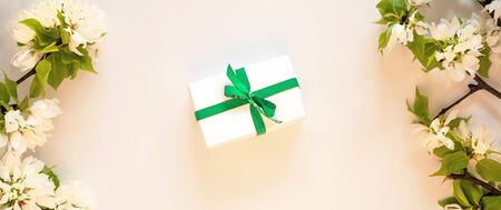 Gift present box apple tree blossom branch white background flat lay. Flowering buds top view template long web banner. Copy space backdrop mockup design. Floral spring flowers green gift box conceptの写真素材