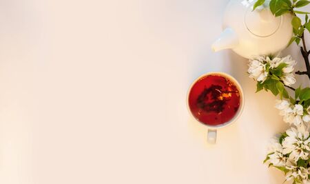 White tea pot, red fruit tea, apple tree blossom, white background flat lay. Tea time top view template long web banner. Copy space backdrop mockup design. Floral spring flowers conceptの写真素材