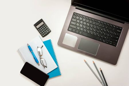 Home office table with laptop and blue notebook on white tableの写真素材