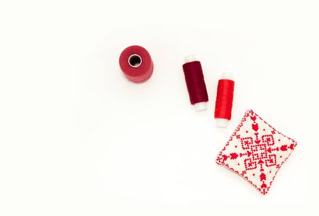 Flat lay with handmade red embroidered needle pad, thread spools, pins, needles, mock up, top view. Layout mockup on blank white background for needlework, sewing poster, banner. Empty space for text.の写真素材